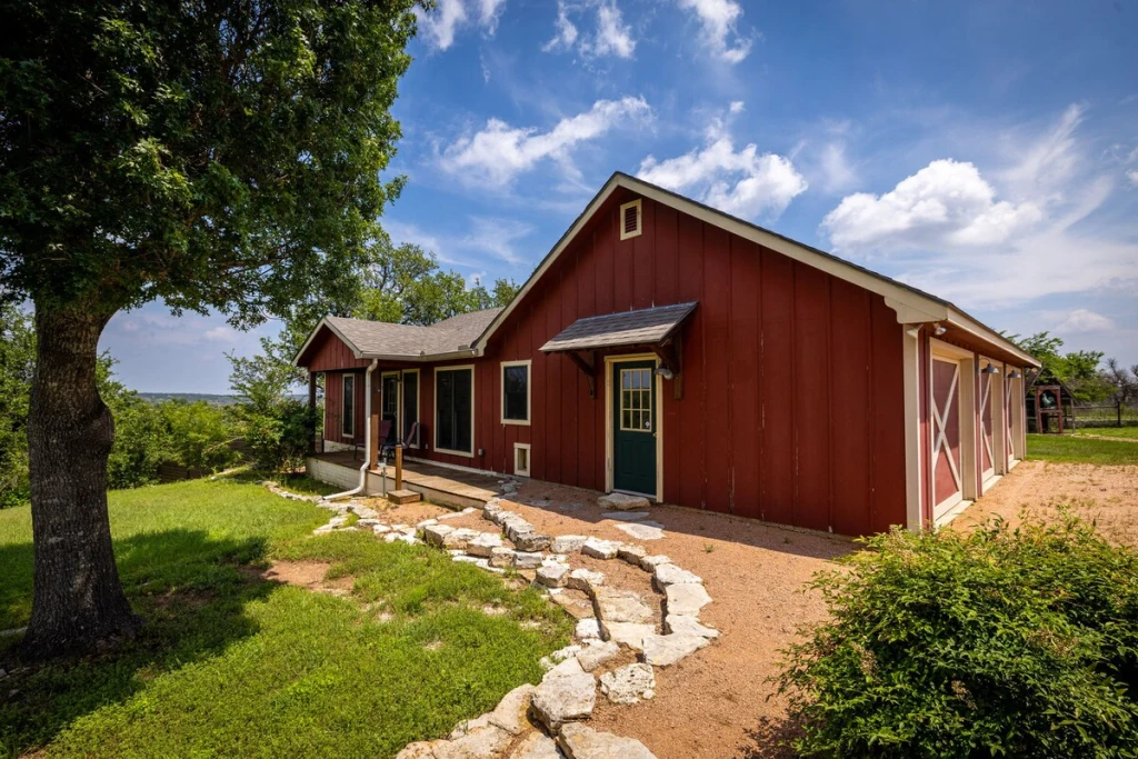Barn House exterior — red barn with green door and stone path, shaded by a mature oak