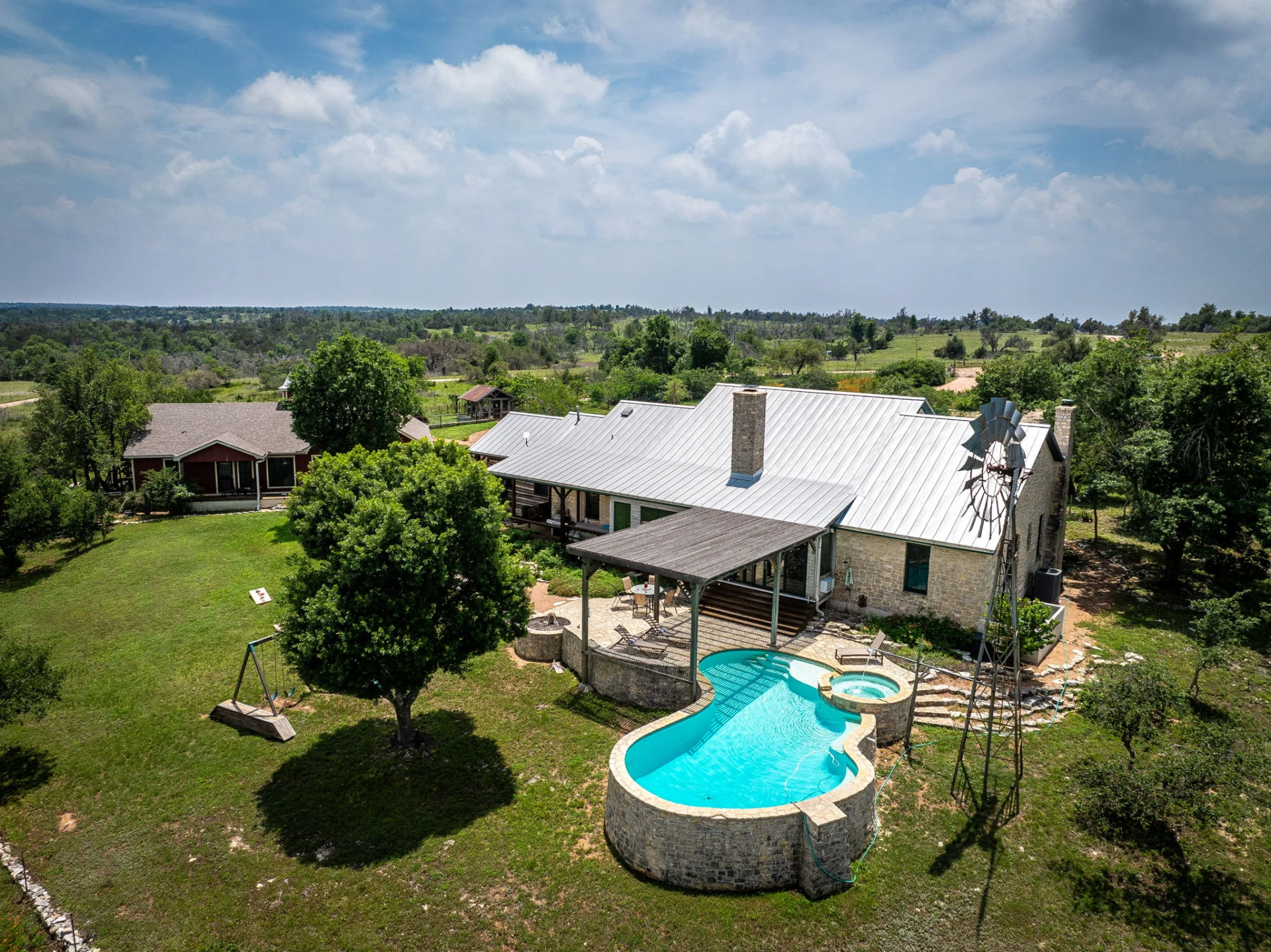 Aerial view of Adobe Creek Ranch in Fredericksburg, Texas — pool, windmill, Main House, and Cowgirl Cabin across 25 Hill Country acres