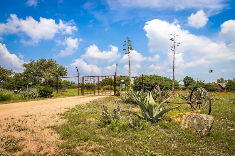Property entry gate framed by agaves and big Hill Country sky